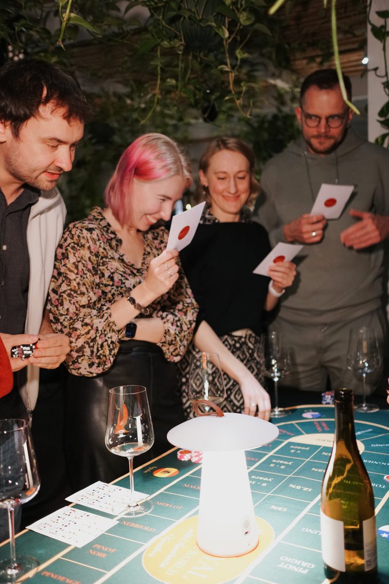 Guests holding tasting cards and chips, laughing around the green Sip Royal table